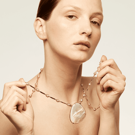 Collar compuesto por una fina cadena bañada en oro, adornada con cuentas de color perla envueltas en una delicada red metálica y un gran colgante con nácar.
