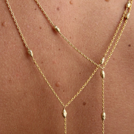 Collar corbatero con cadena rectangular en oro 14K gold filled, acentuado con 10 cuentas orzo texturizadas en el mismo acabado. Su caída aporta longitud y define el escote con un gesto sutil y marcado.