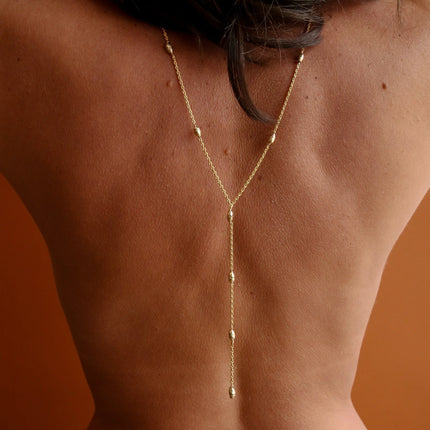 Hermoso Collar corbatero con cadena rectangular en oro 14K gold filled, acentuado con 10 cuentas orzo texturizadas en el mismo acabado. Su caída aporta longitud y define el escote con un gesto sutil y marcado.
