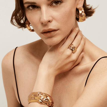 Brazalete de compresión bañado en oro fino, con un efecto comprimido, como si estuviera esculpido en oro. Talla ajustable.