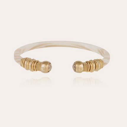 Una fina pulsera de acetato, forrada a mano con finos hilos chapados en oro e hilos de colores. Esta pulsera termina con dos bolas adornadas con pedrería. 